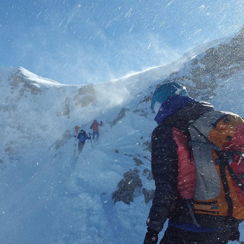 Three hikers with ski backpacks scaling a snow-capped mountain.