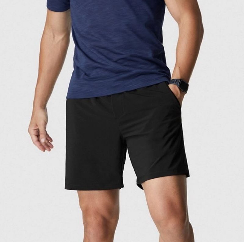 A man with his hand in his pocket is wearing a watch, blue shirt, and a pair of Fabletics Men The Franchise Short.