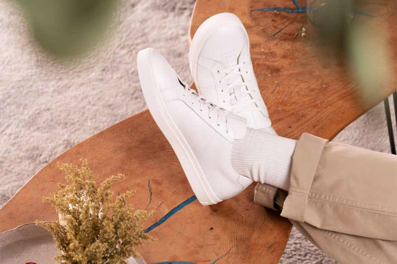 A figure wearing Greats Royale Blanco Sneakers propped on a table.