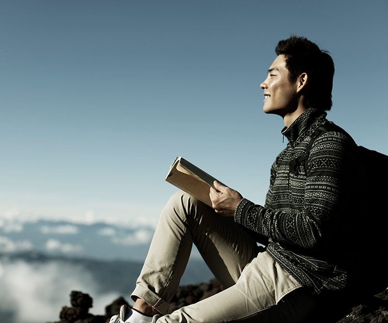 Young man reading a book in the mountains