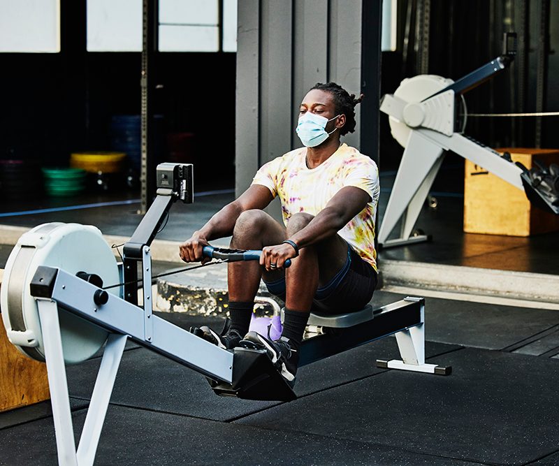 Man wearing protective face mask working out on rowing machine at outdoor gym