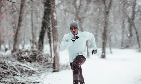 Man dressed in winter clothes running under the snowy weather.