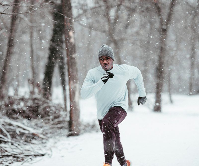 Man dressed in winter clothes running under the snowy weather.