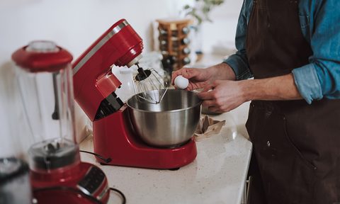 Person cracking egg on the bowl of electric stand mixer