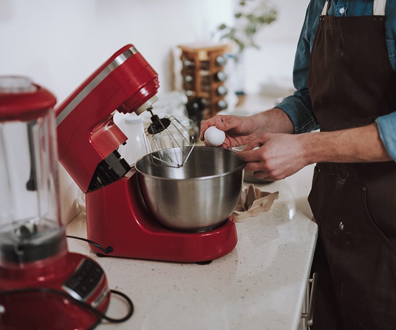 Person cracking egg on the bowl of electric stand mixer
