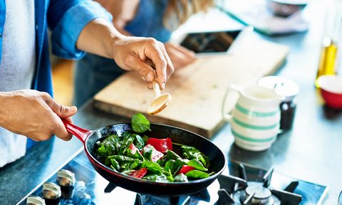 Close-up of a man holding frying pan with fresh vegetables and a wooden spoon