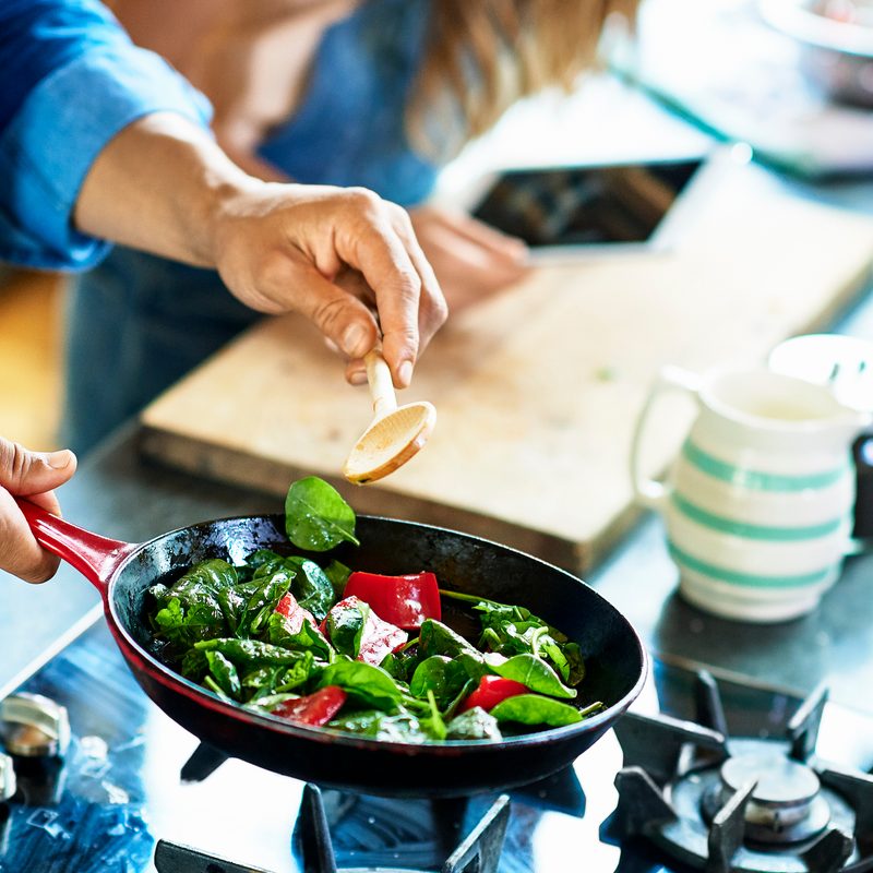 Close-up of a man holding frying pan with fresh vegetables and a wooden spoon