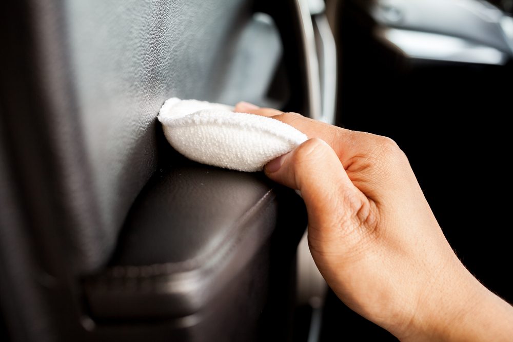 Closeup of a hand wiping the inside of a car door with a leather care product.