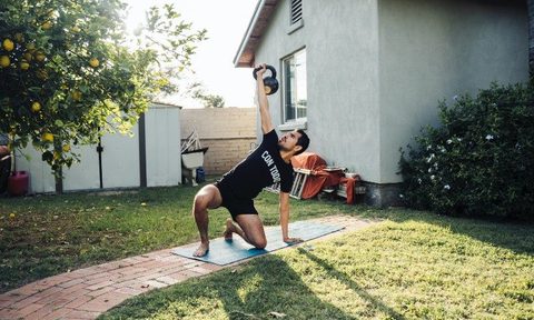 Man lifting a kettlebell on a yoga mat outside