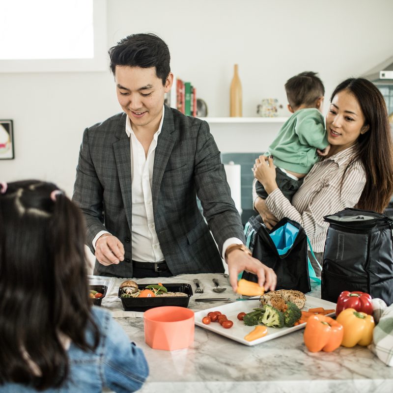 A family of four is preparing a meal in the kitchen for their father's lunchbox.