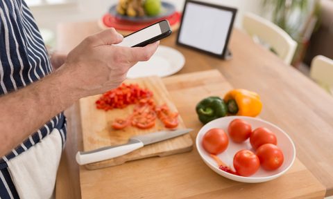Man using smartphone while preparing food in the kitchen