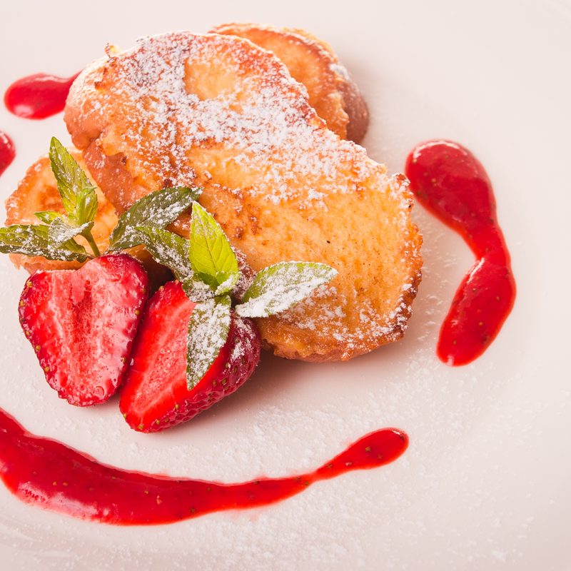 French toast with strawberries and powdered sugar on a white plate