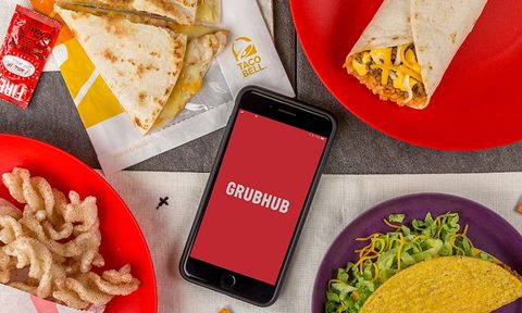 A phone displaying Grubhub logo while surrounded by food.