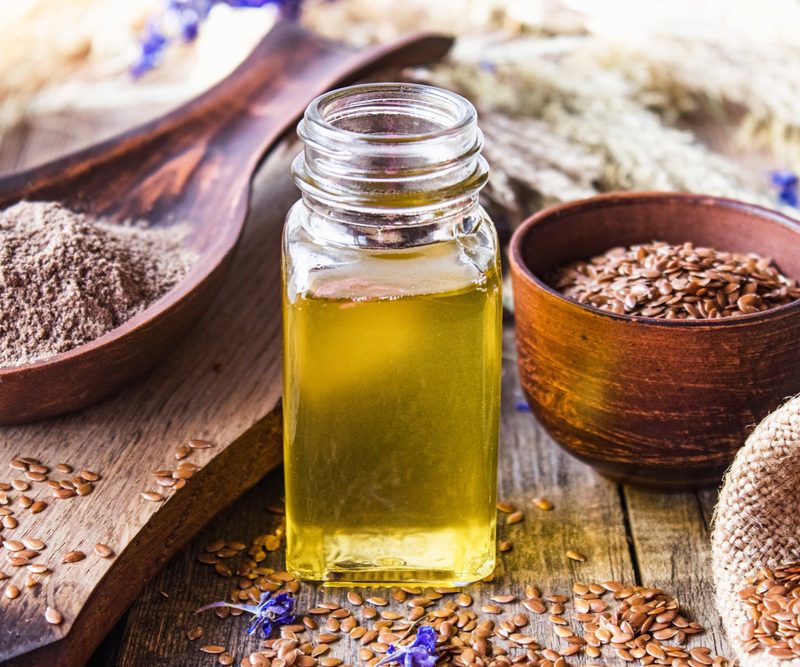 Flaxseed oil in a bottle near flaxseed on a wooden table.