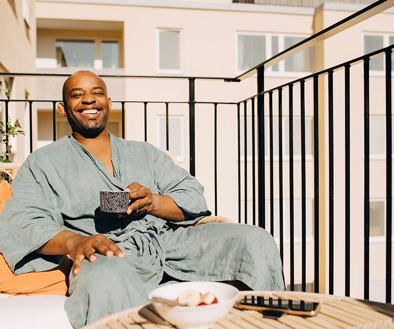 Happy mature man having coffee while sitting on a sofa on a balcony