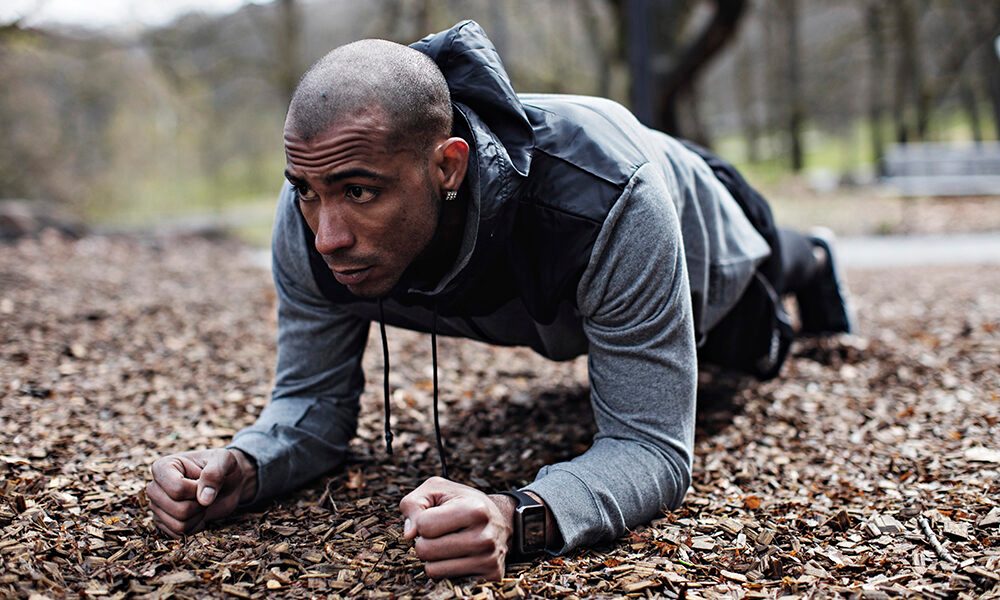 Determined male athlete performing plank position in forest.