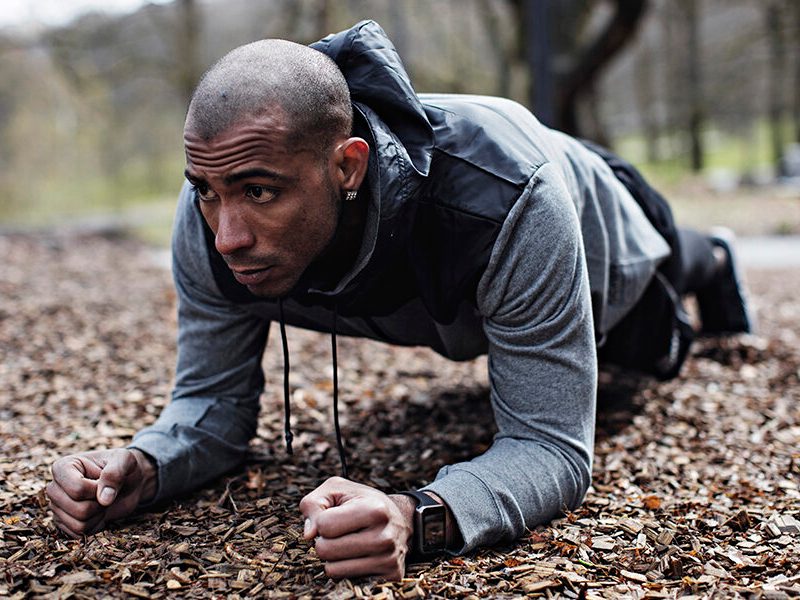 Determined male athlete performing plank position in forest.