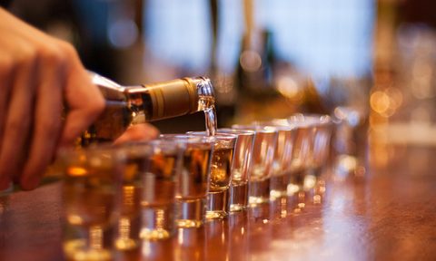 Person pouring a line of shots in a bar