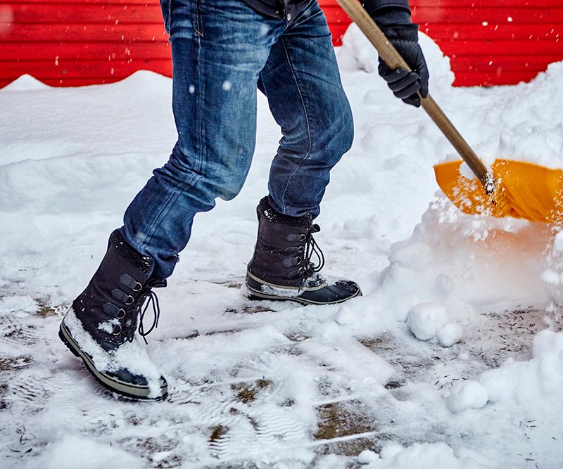 A person using a yellow snow shovel to clear up snow.