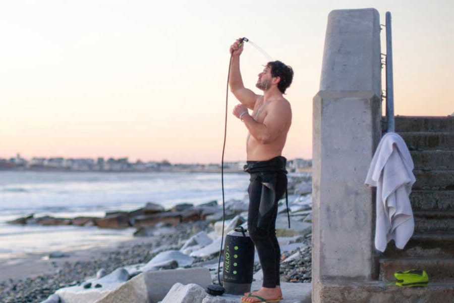 Man using a portable outdoor shower near the beach.