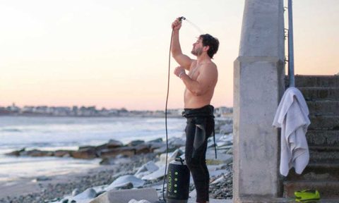 Man using a portable outdoor shower near the beach.
