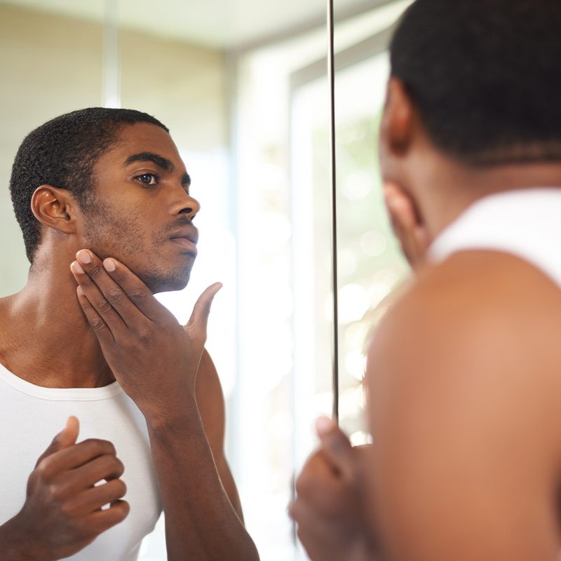 Guy looking at his skin in mirror.