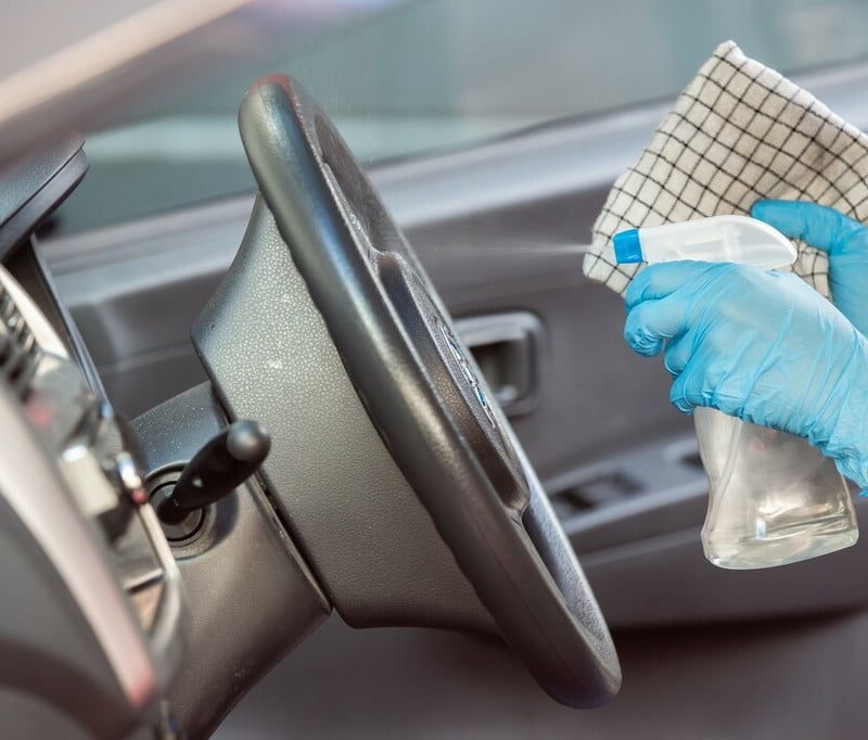 A person wearing gloves spraying a cleaner on the steering wheel.