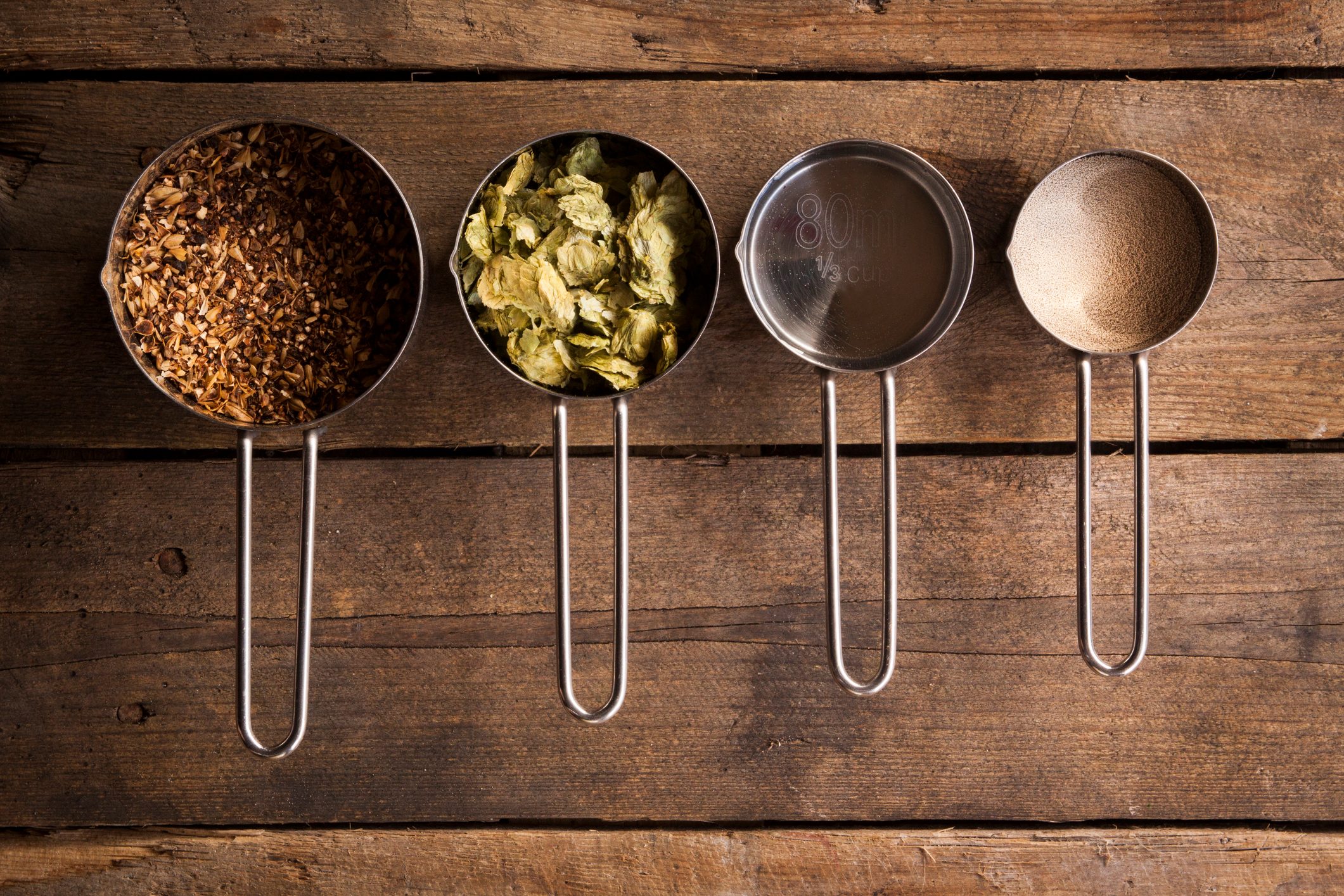 An overhead shot of a collection of basic home-brew beer ingredients, sitting on a rustic wooden background