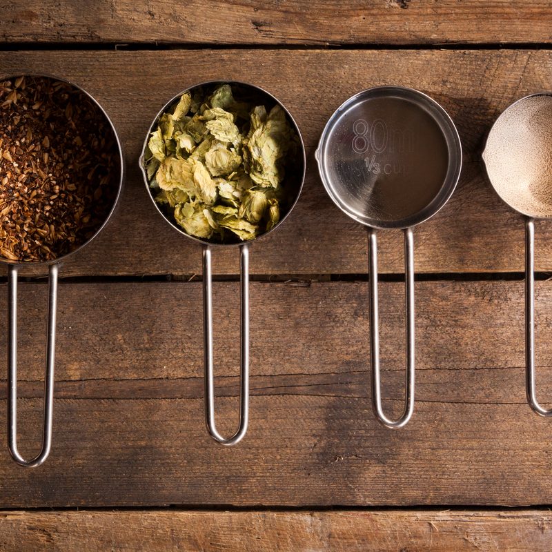 An overhead shot of a collection of basic home-brew beer ingredients, sitting on a rustic wooden background