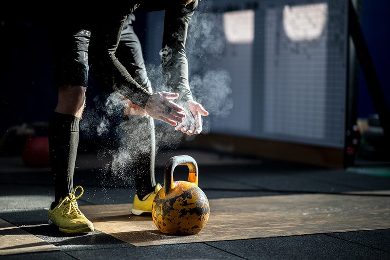 Person chalking up their hands standing bent over behind a kettlebell in a gym.