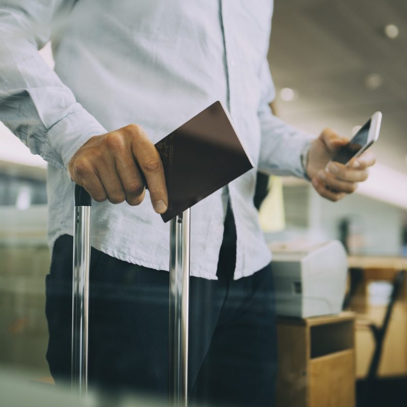 Person holding passport and luggage at the airport.
