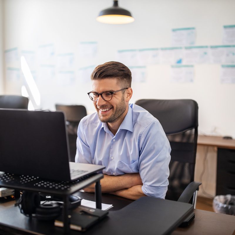 An enthusiastic man wearing glasses while viewing his laptop perched on a riser.