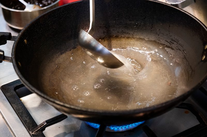 Slow cooked clear beef bone broth or stock without meat in cooking pot on dark rustic background, top view.