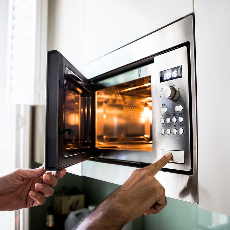 Someone lifting something out of a built-in microwave.