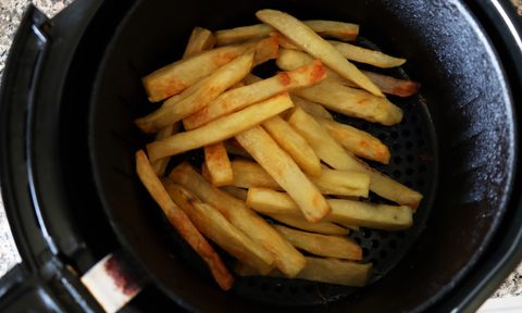 Inside of an air fryer with a pile of golden brown, freshly cooked French fries