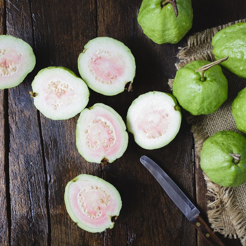 whole and sliced Guava fruit sitting next to a knife on a wooden table.
