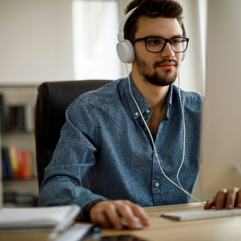 A man wearing glasses and headphones while browsing on his desktop.