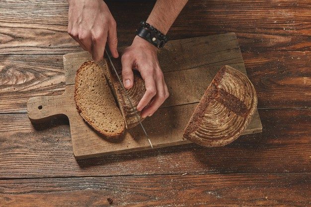Man slicing freshly baked organic bread on a wooden cutting board
