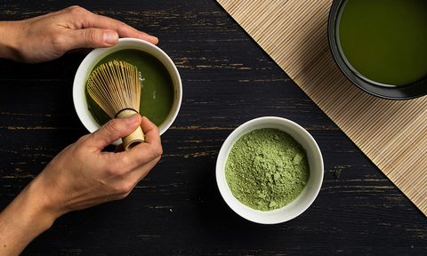 what is matcha woman s hands mixing green tea powder in a bowl  overhead view