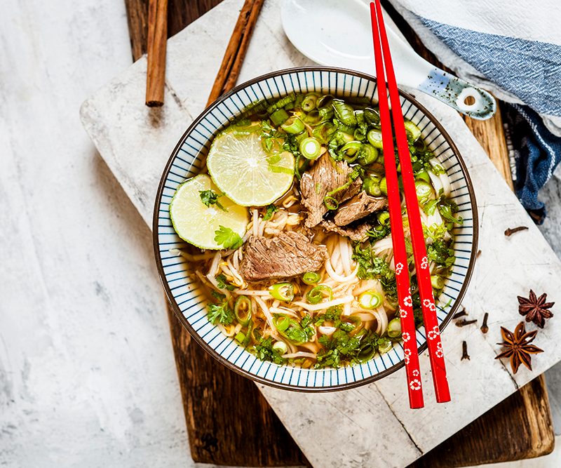 Bowl of Vietnamese Pho with rice noodles, mung beans, cilantro, spring onions and limes