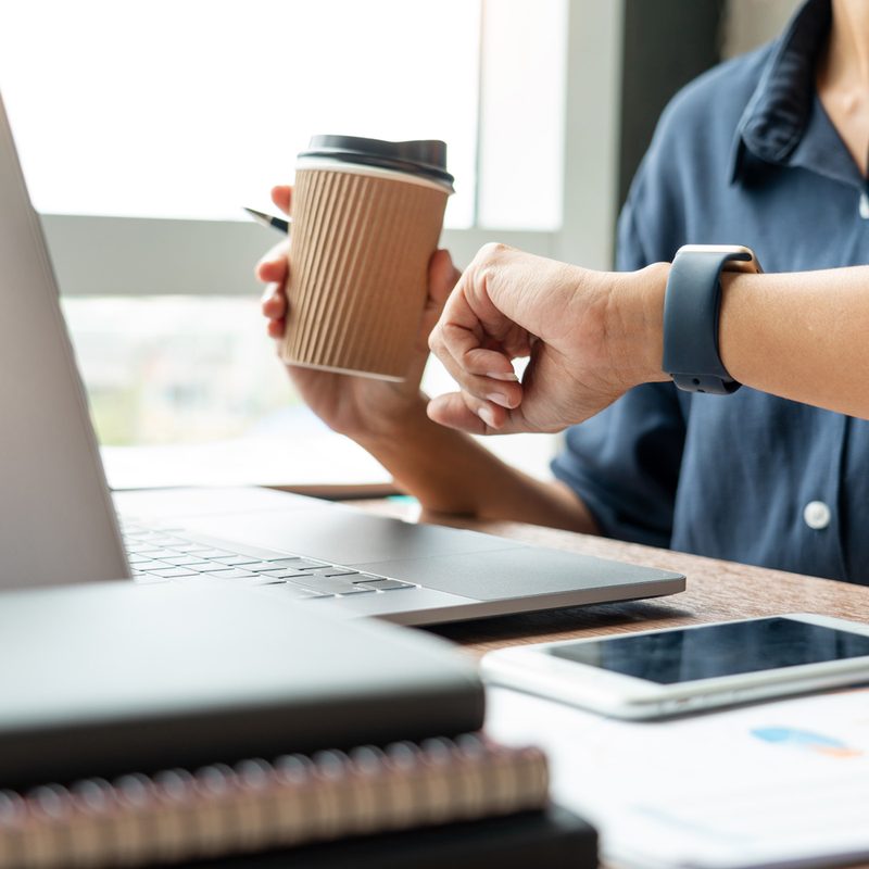 Close-up shot of a man holding a cup of coffee while checking the time on his watch.