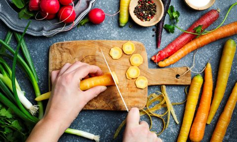 Cutting carrots on wooden board and fresh spring vegetables for vegetarian cooking on the table, top view.