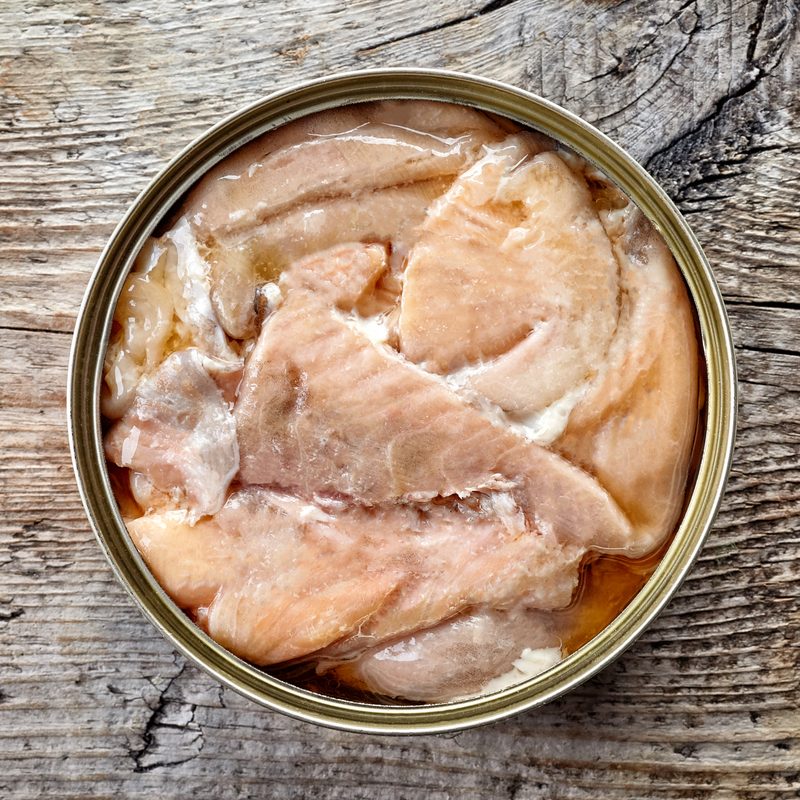 Open tin can, canned salmon, on wooden background, top view