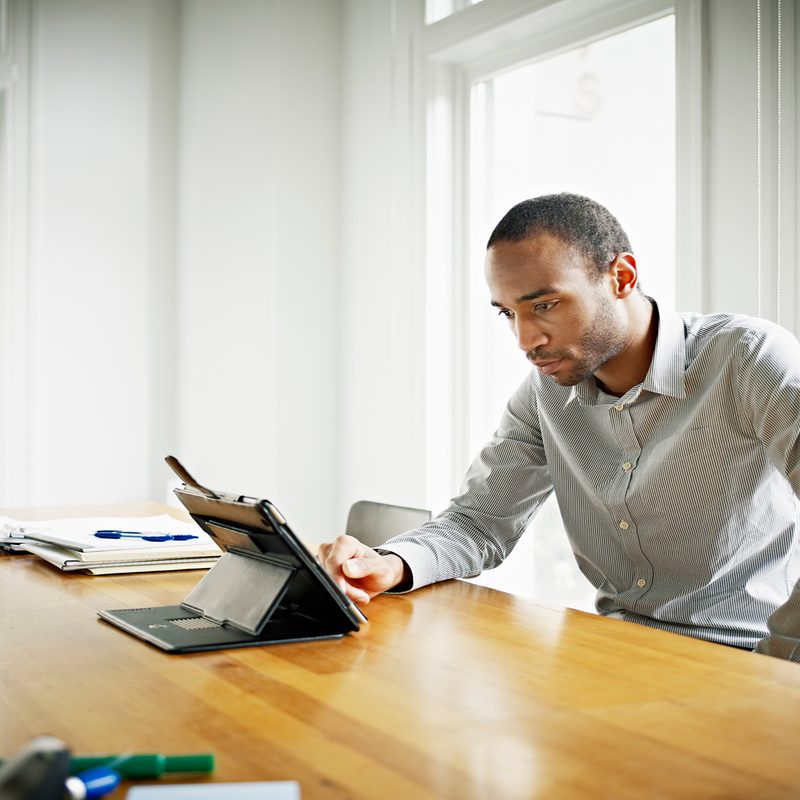 A man wearing a work shirt as he uses his iPad.