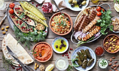 Middle Eastern, Arabic, or Mediterranean dinner table with grilled lamb kebab, chicken skewers with roasted vegetables and appetizers variety serving on rustic outdoor table