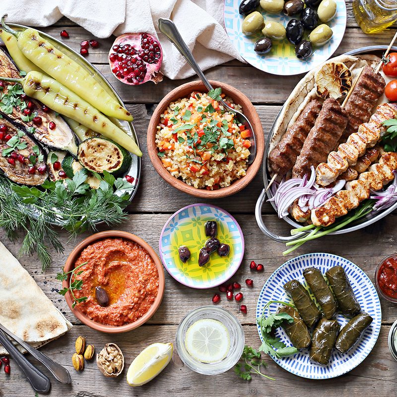 Middle Eastern, Arabic, or Mediterranean dinner table with grilled lamb kebab, chicken skewers with roasted vegetables and appetizers variety serving on rustic outdoor table