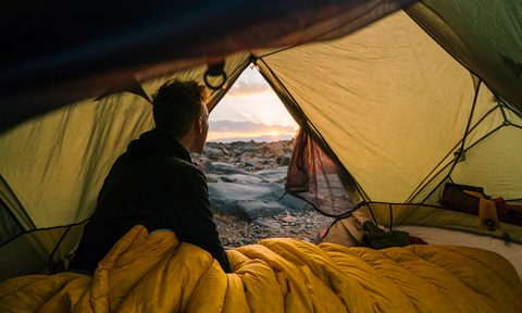 Camping looking out his tent door in a sleeping bag