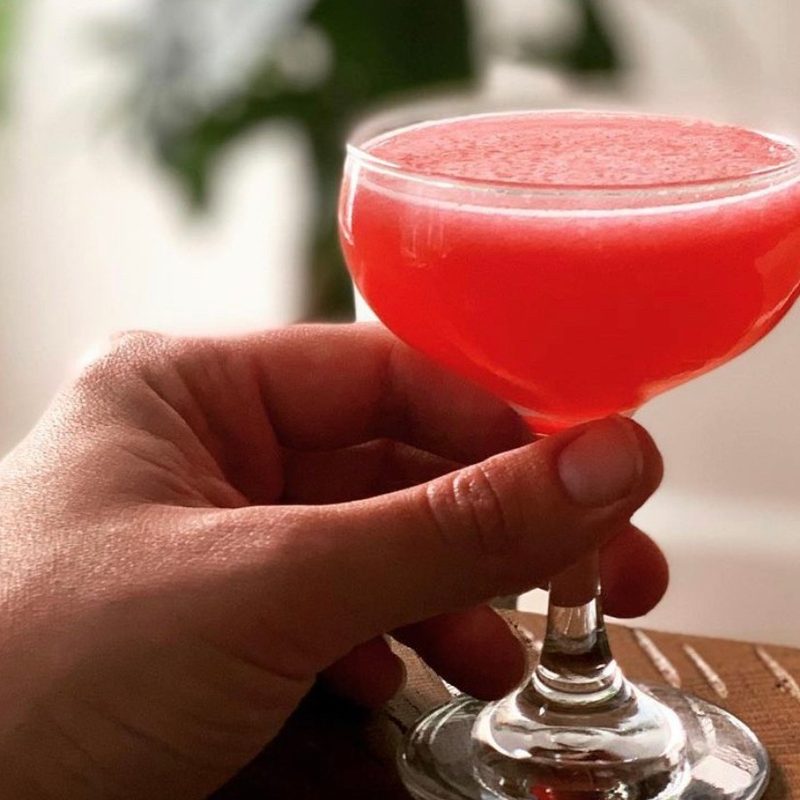 A hand holding a glass of blackberry mint daiquiri on a wooden table