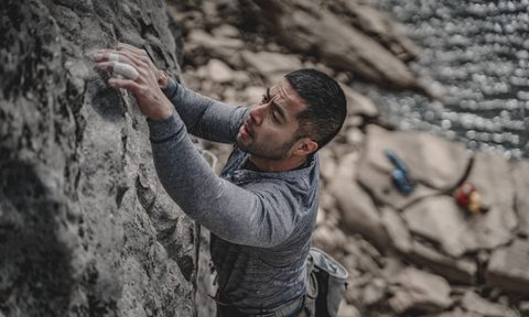 A man in gray long-sleeved shirt climbing a rock formation by a body of water