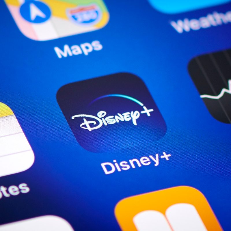 The Disney Plus app icon surrounded by other iOS apps on an iphone.